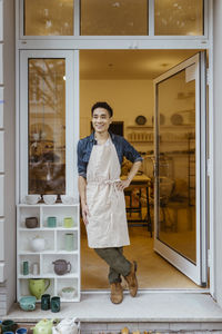 Happy male owner looking away while standing at doorway of pottery shop