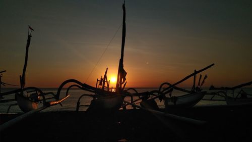Silhouette sailboats moored on beach against sky during sunset