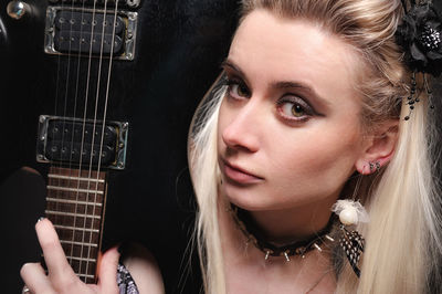 Close-up portrait of young woman with electric guitar against black background