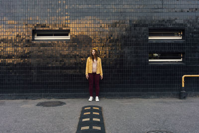 Young woman standing on footpath in front of black wall