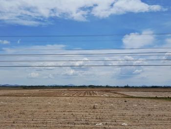 Electricity pylon on field against cloudy sky