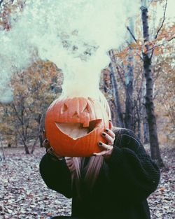 Person holding pumpkin against tree trunk during halloween