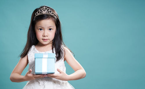 Portrait of cute girl holding gift while standing against blue background