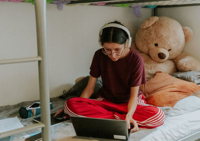 A teenage girl sits on a bed with a computer.