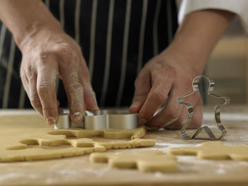 Midsection of chef cutting dough with pastry cutter at table