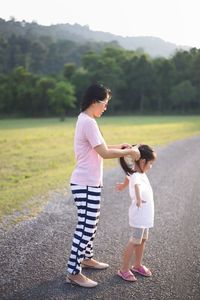 Mother tying hair of daughter while standing on road
