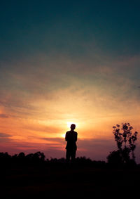 Silhouette man standing on field against sky during sunset