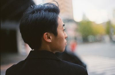 Close-up of young man looking away while standing on street in city