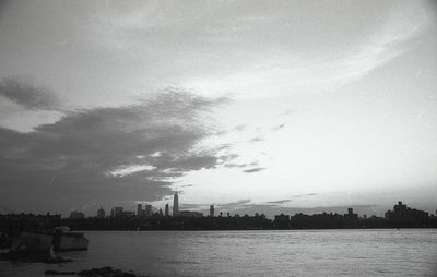 View of city at waterfront against cloudy sky