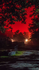 Illuminated street amidst field against sky at night