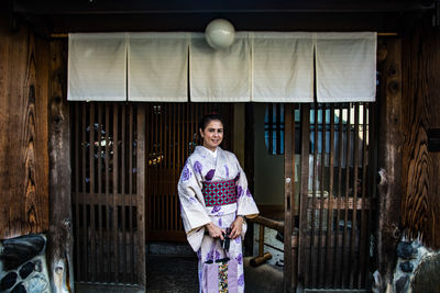 Portrait of smiling young woman standing against wall