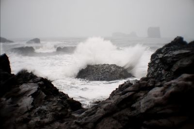 Scenic view of waves breaking on rocks against sky