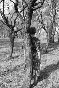 Rear view of woman standing by trees in forest