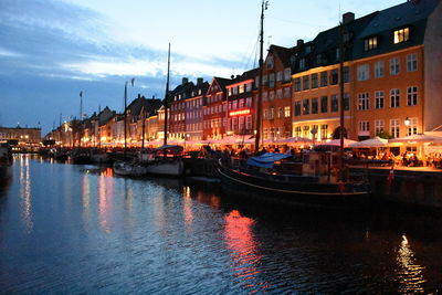 Sailboats moored on canal in city against sky at dusk