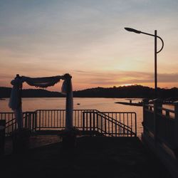 Silhouette street light in front of building against sky during sunset