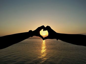 Cropped image of hands making heart shape against sea at beach