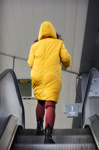 Young woman in yellow hood jacket using escalator