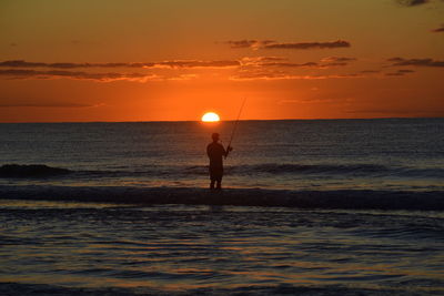 Silhouette man standing on beach against sky during sunset