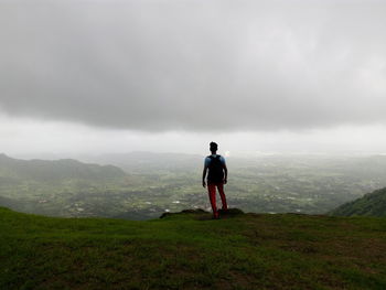 Rear view of man standing on mountain against cloudy sky