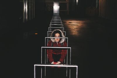 Portrait of girl sitting by bicycle rack in parking lot at night