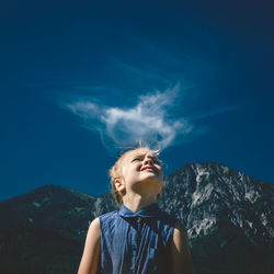 Girl looking up at blue sky with mountain backdrop and cloud above