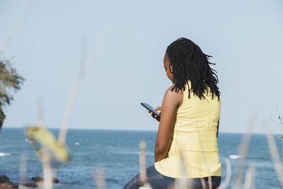 Rear view of woman using mobile phone by sea against sky