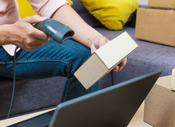 Midsection of man scanning boxes while sitting on sofa at home