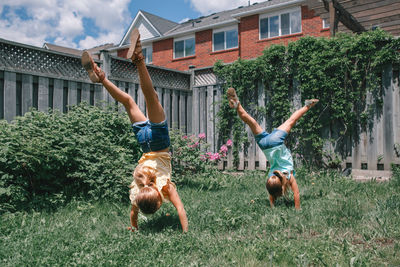 Full length of girls doing handstand in yard