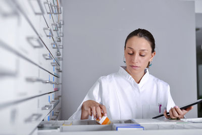 Woman wearing lab coat while looking in drawer of cabinet