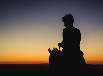Silhouette man on horse against clear sky during sunset