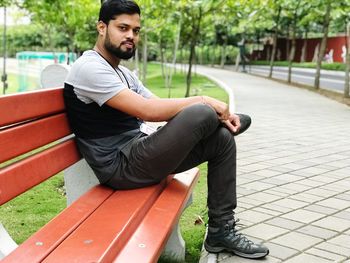 Portrait of young man sitting on bench in park