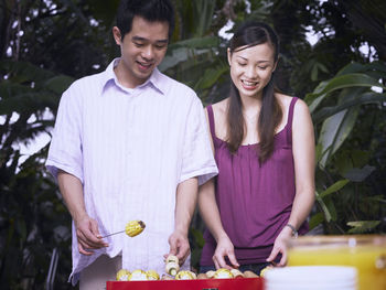 Young couple preparing food on barbecue grill against swimming pool