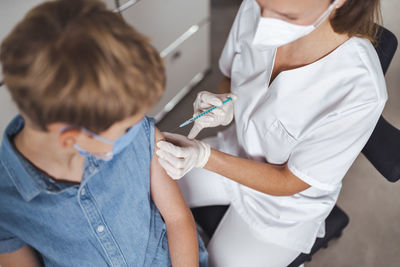 Nurse in protective face mask administering boy with covid-19 vaccine