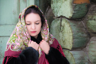 Woman wearing scarf standing against wooden wall