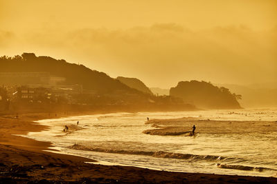 Scenic view of surfer beach against orange sky during sunrise