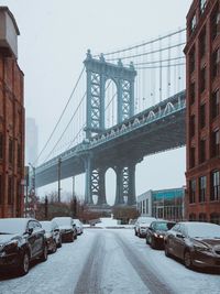 Cars on snow covered street against manhattan bridge in city