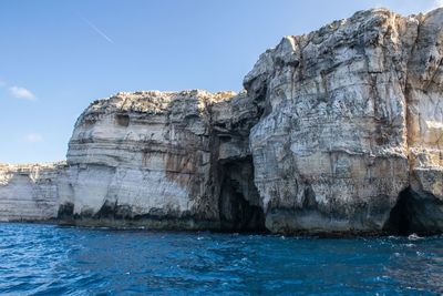 Rock formations by sea against blue sky