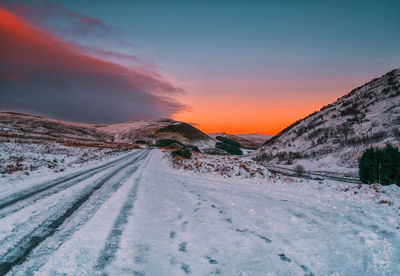 Snow covered road against sky during sunset