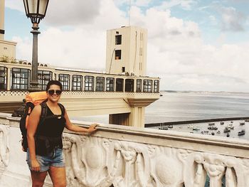 Full length of young woman standing on railing against sea