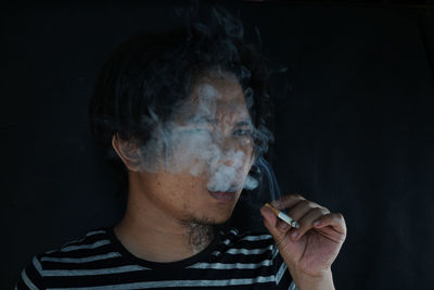 Close-up of man smoking cigarette against black background