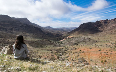 Rear view of girl sitting on landscape against sky