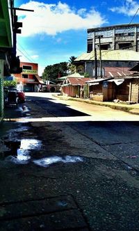 Wet street by houses in town against sky