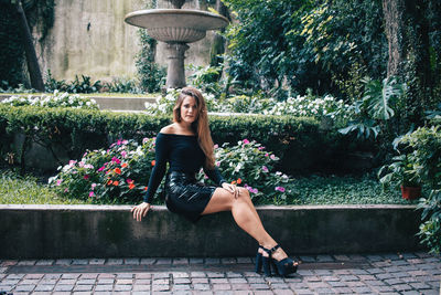 Full length portrait of woman sitting against wall