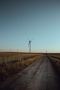 Road amidst field against clear sky. windmill. 