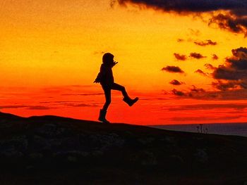 Silhouette man jumping on land against orange sky