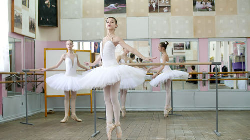 In ballet hall, girls in white ballet skirts are engaged at ballet, rehearse turning