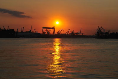 Silhouette cranes at commercial dock against sky during sunset