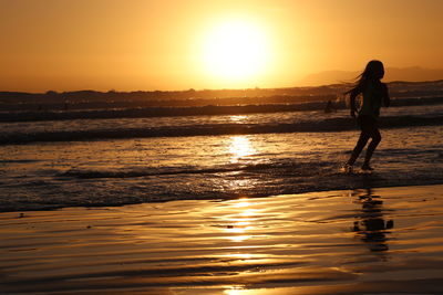 Silhouette girl on beach against sky during sunset