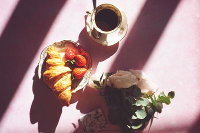 Directly above of a cup of coffee, a croissant and  flowers on pink background
