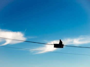 Low angle view of silhouette person in overhead cable car against sky